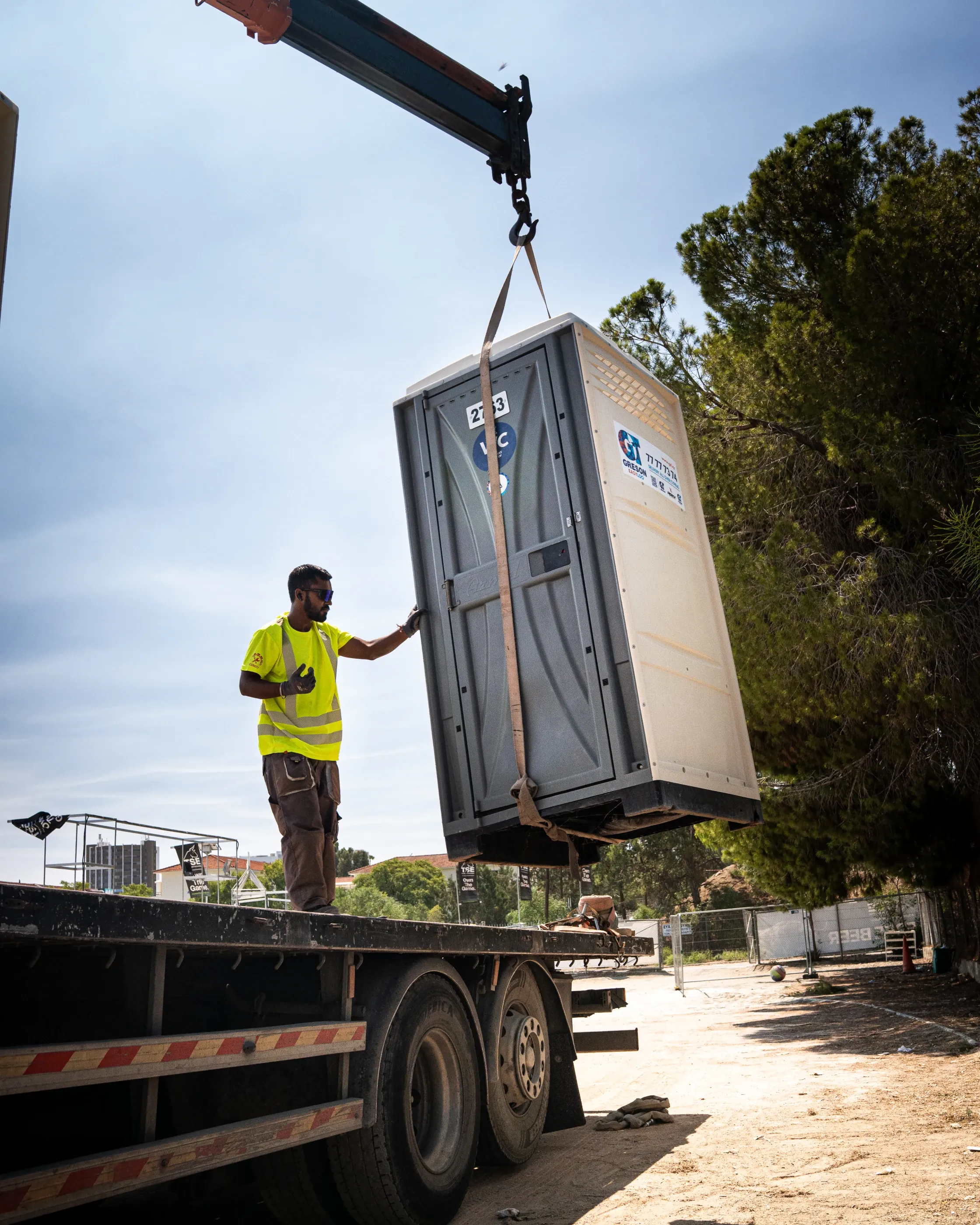 Greson Easy Loo crew member guiding a portable toilet lifted by crane onto a lorry