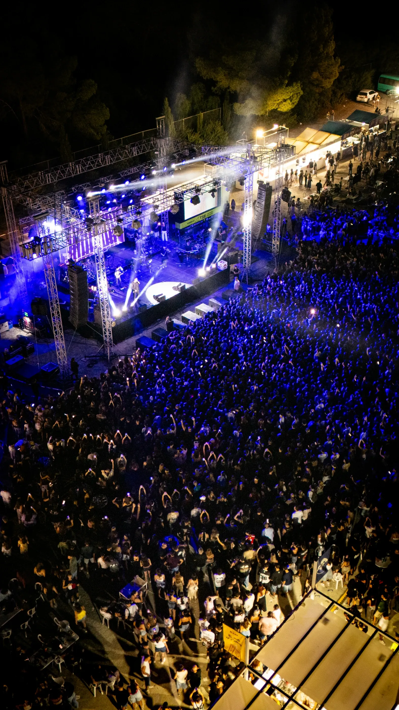 Aerial view of a packed night-time festival crowd in front of a lit stage