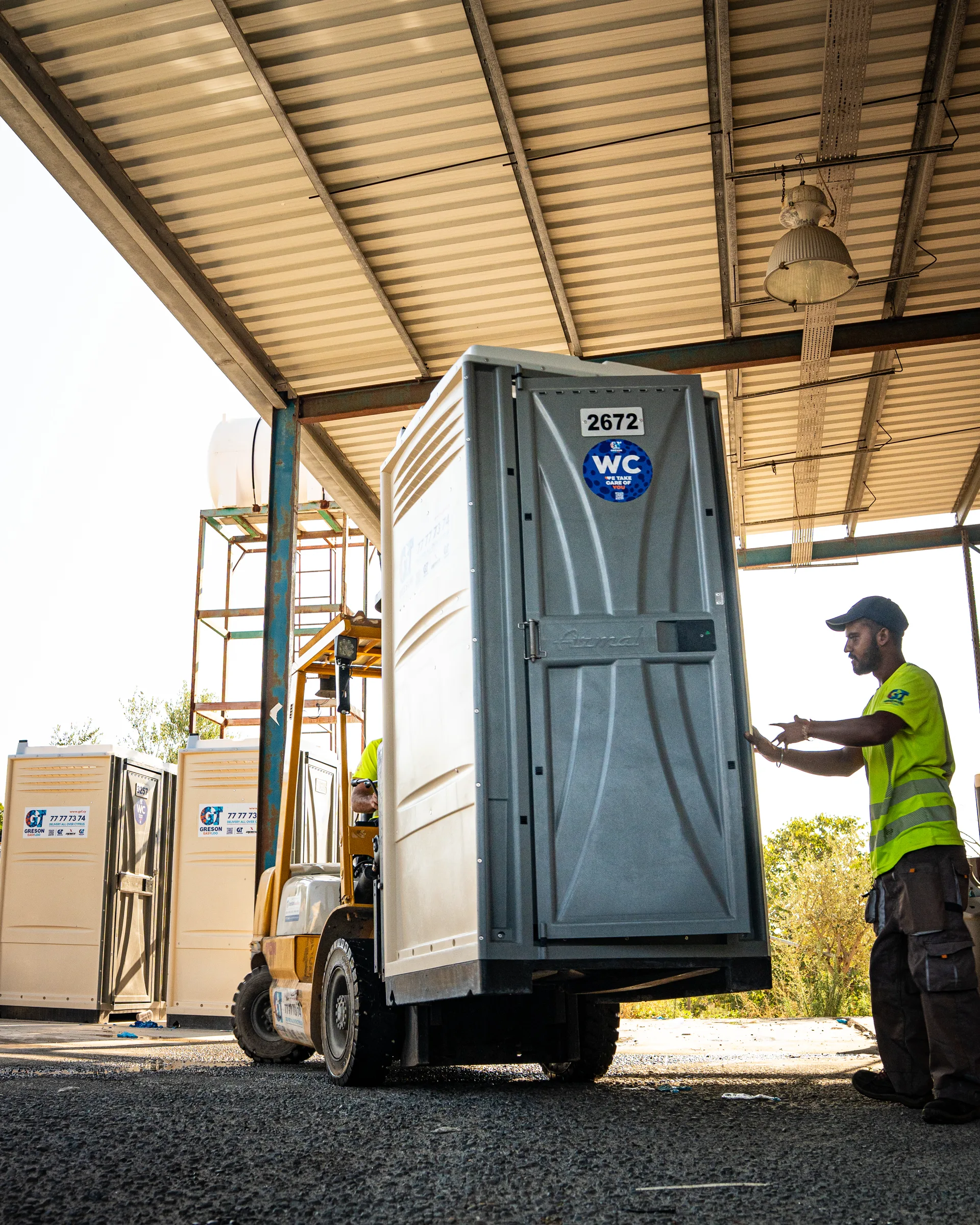 Forklift moving a portable toilet under the yard canopy